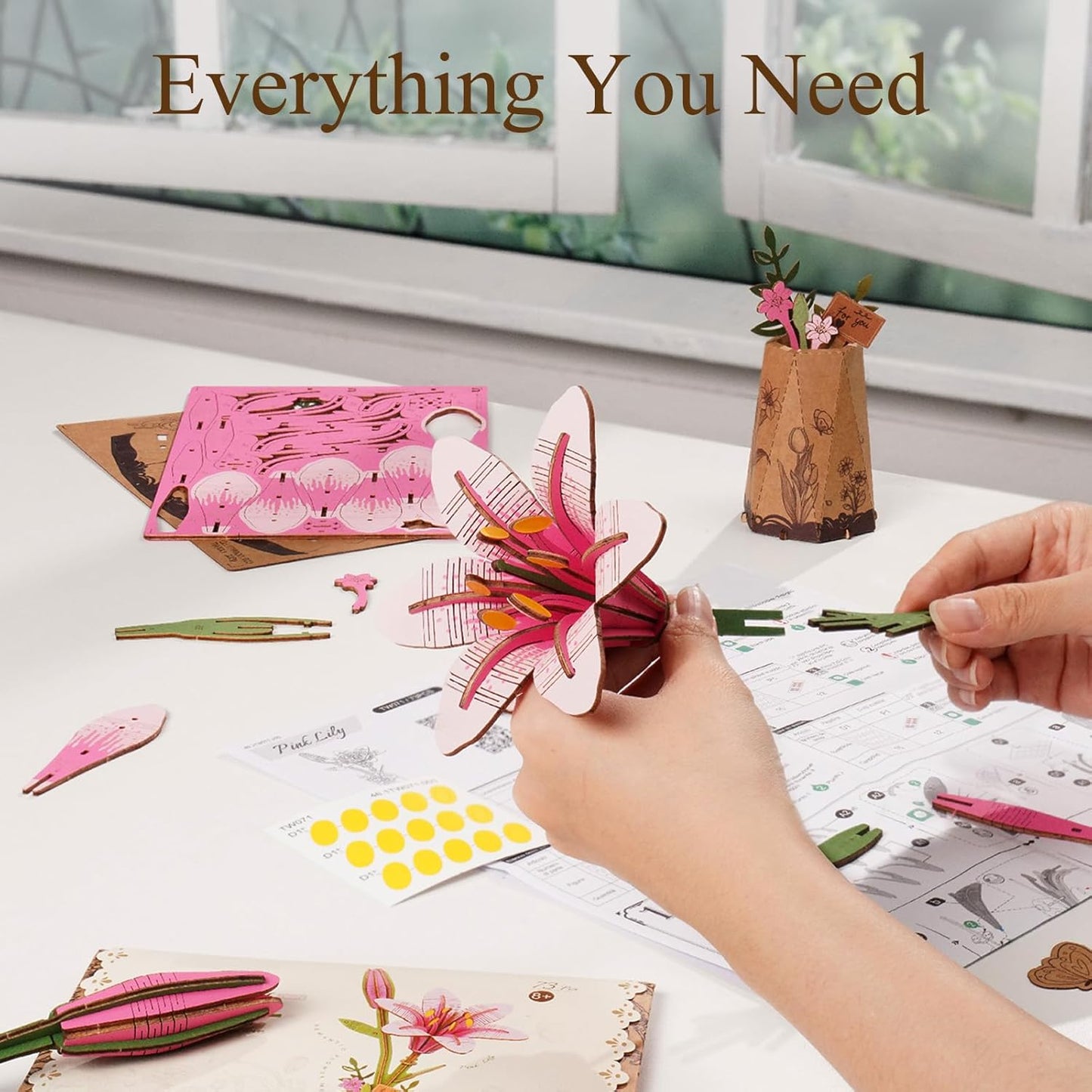 Person holding a 3D paper flower craft with materials and tools on a table.