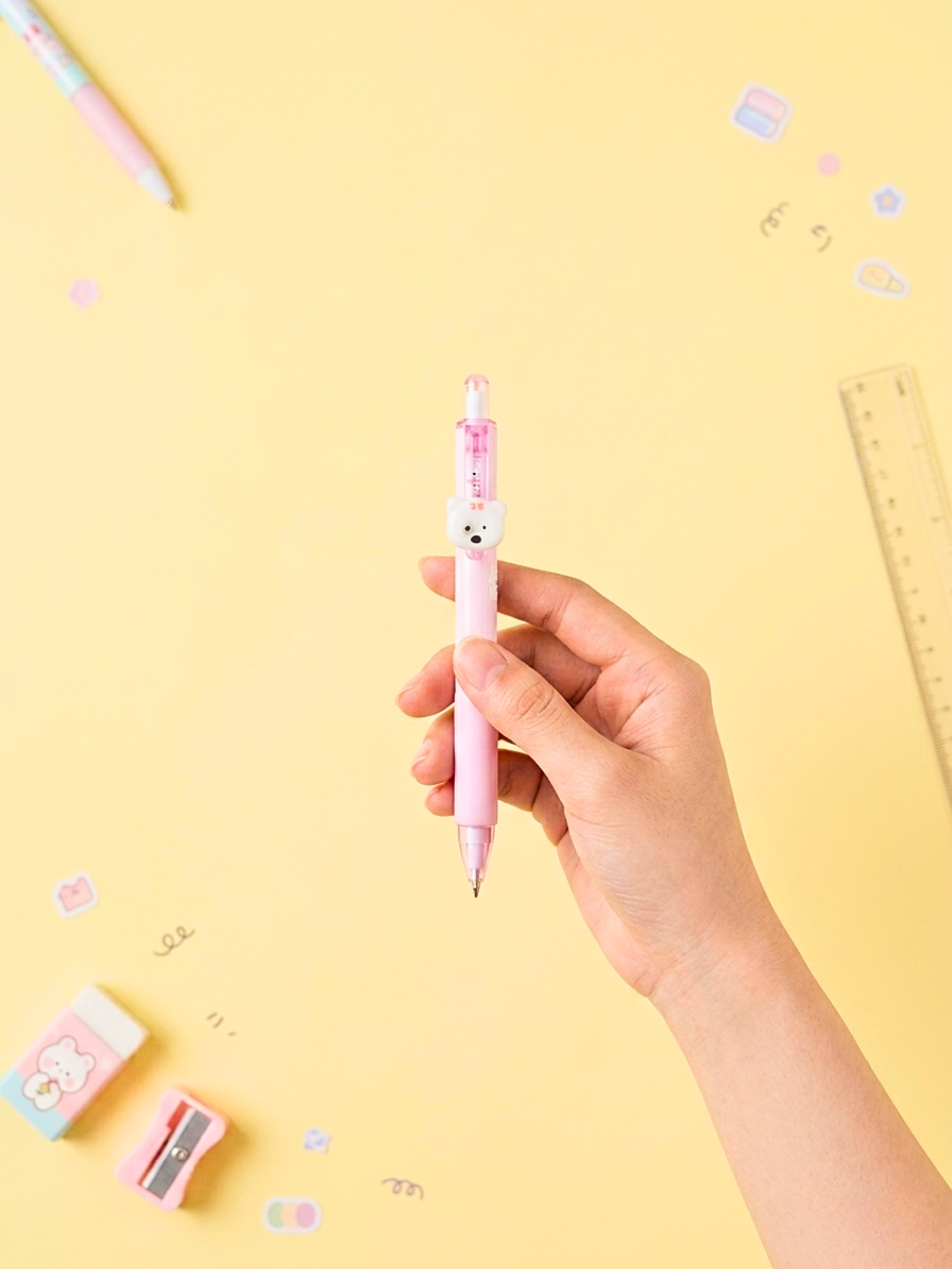 Hand holding a pink pen with a bear design on a yellow background