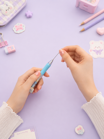 Person holding a small blue pen on a purple surface with stationery items around