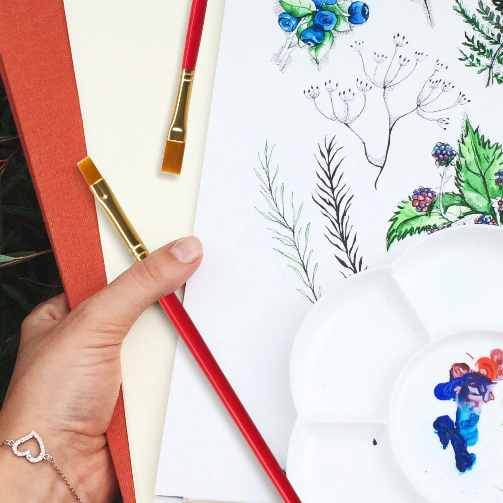Artistic activity with colored pencils, a red book, and a drawing of flowers and leaves on a white surface.