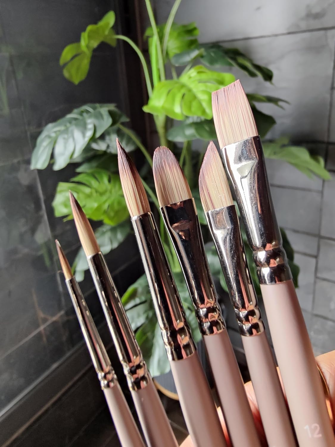 Set of makeup brushes with rose gold accents held against a blurred indoor background