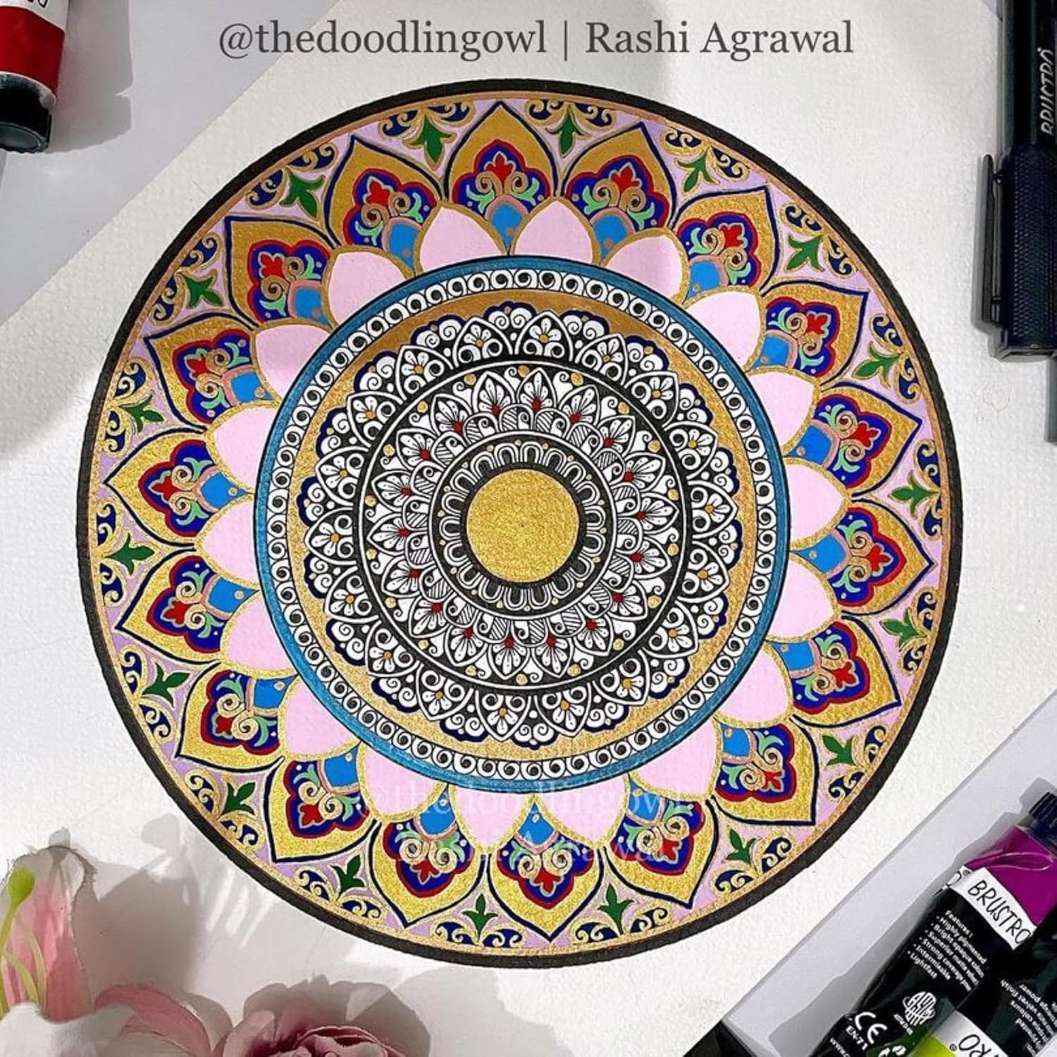 Colorful mandala drawing on a white surface with art supplies around