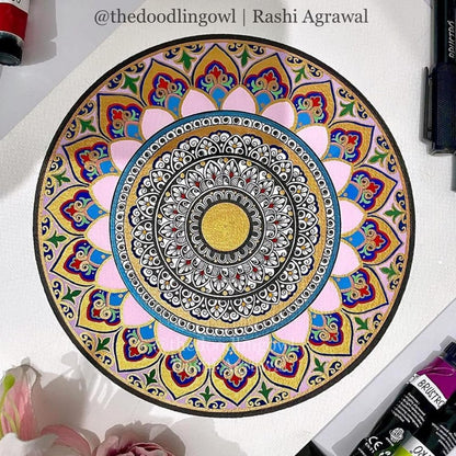 Colorful mandala drawing on a white surface with art supplies around