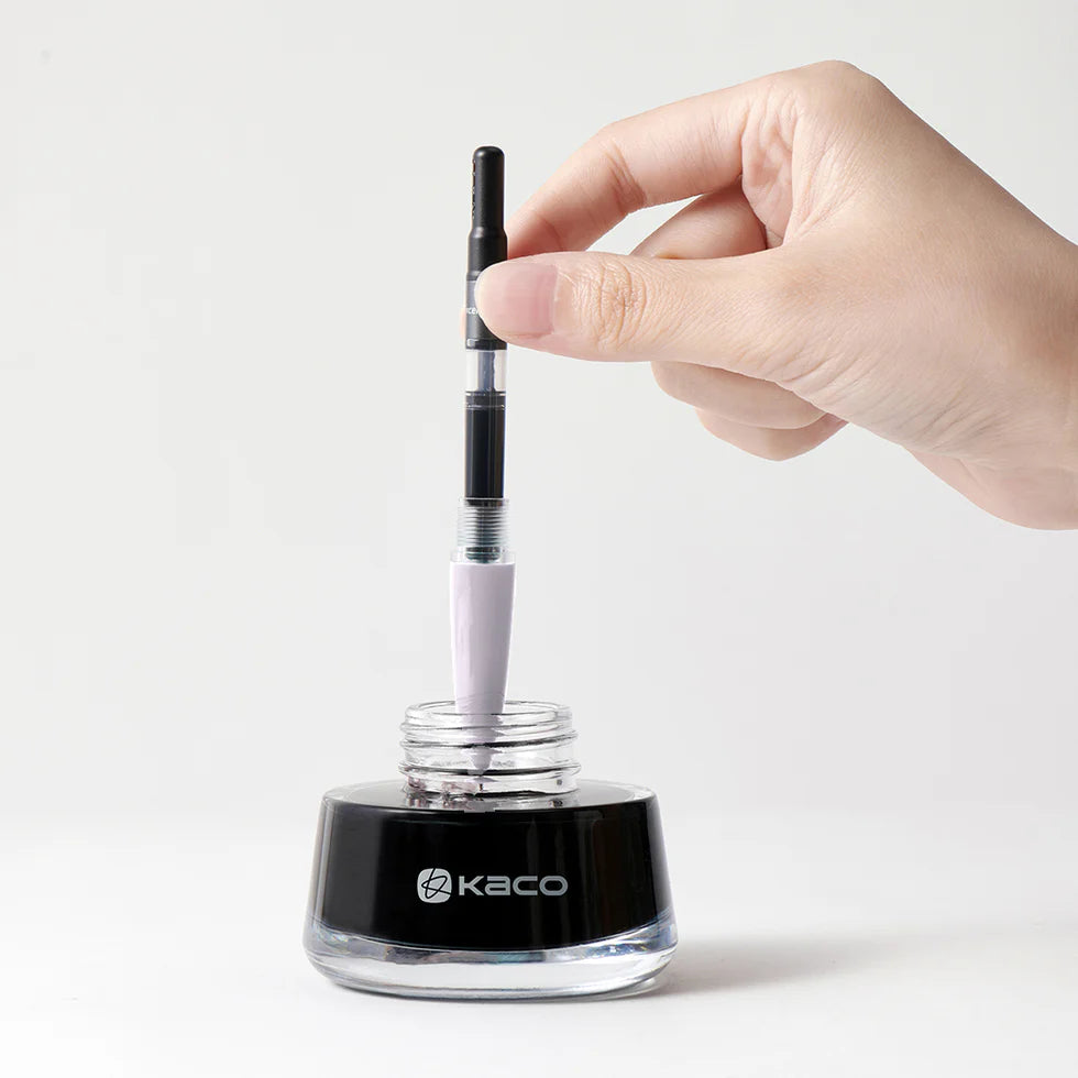 Hand using a Kaco eyeliner pen with a clear container on a white background