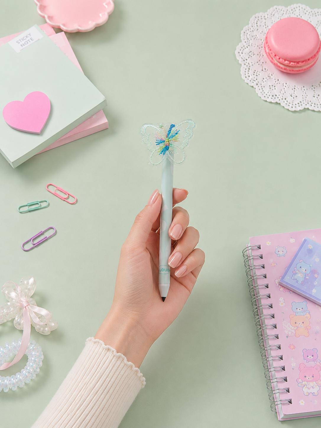 Hand holding a decorative pen with stationery items on a light green background