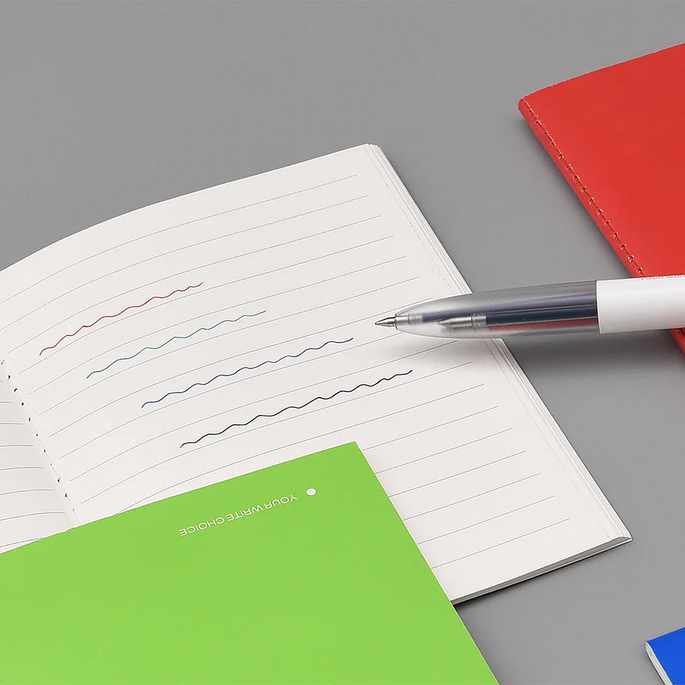 Open notebook with lined pages, a pen, and a red and green notebook on a gray surface.