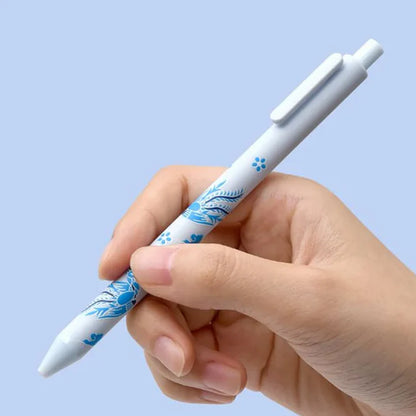 Hand holding a white pen with blue floral design against a light blue background