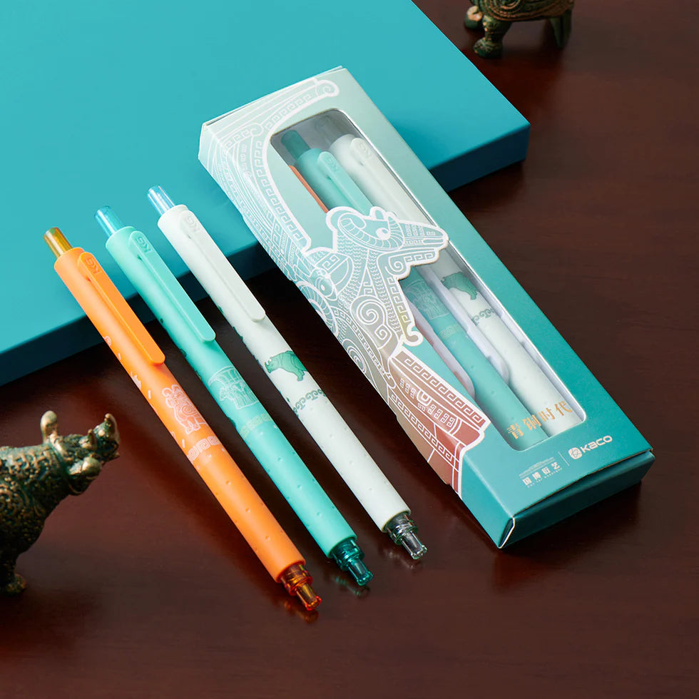 Four pens with different colored caps in front of a branded pen box on a wooden surface.