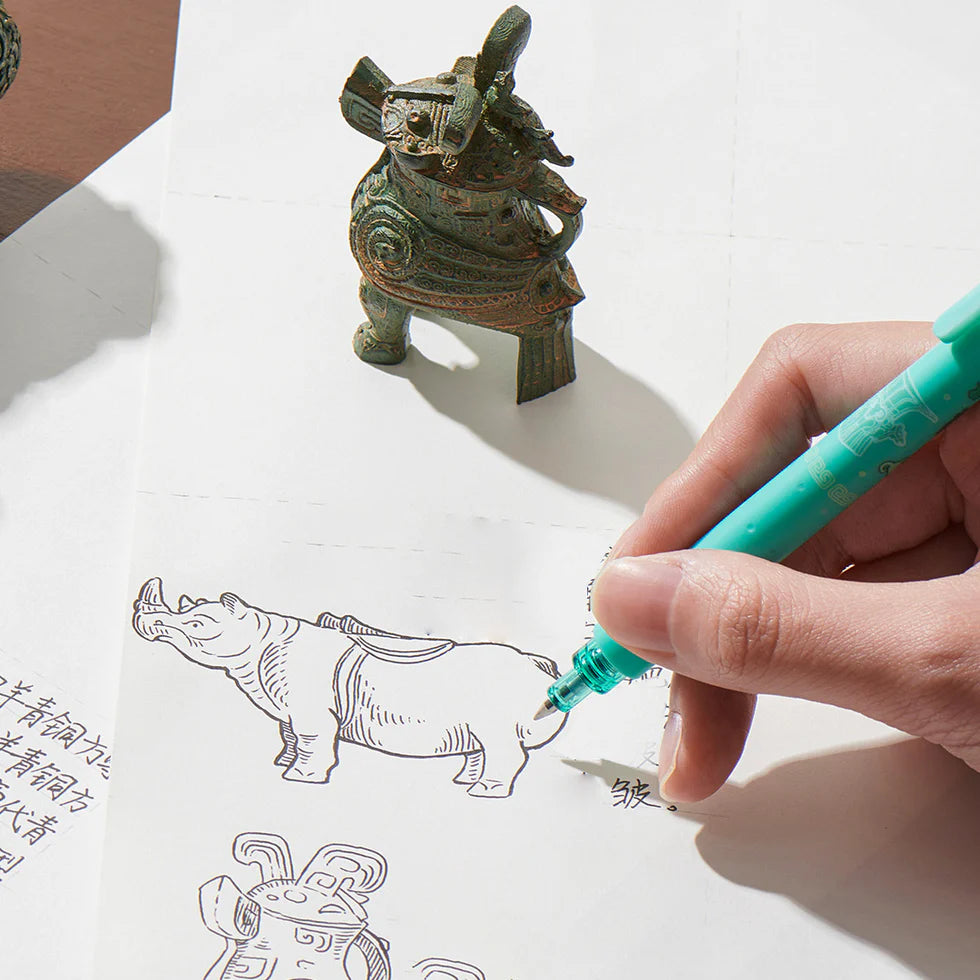 Hand drawing a rhino with a turquoise pen on a white sheet of paper, with a small bronze statue in the background.