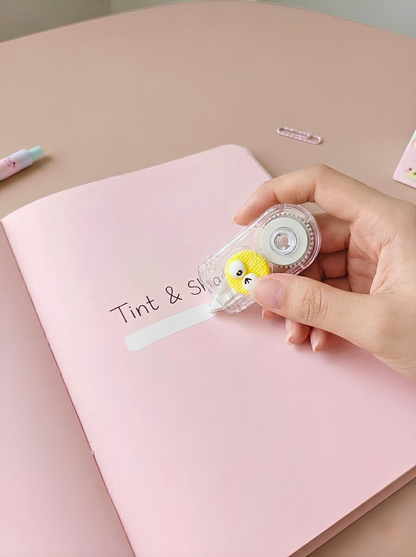 Hand holding a small round object with a cartoon character over a pink notebook.