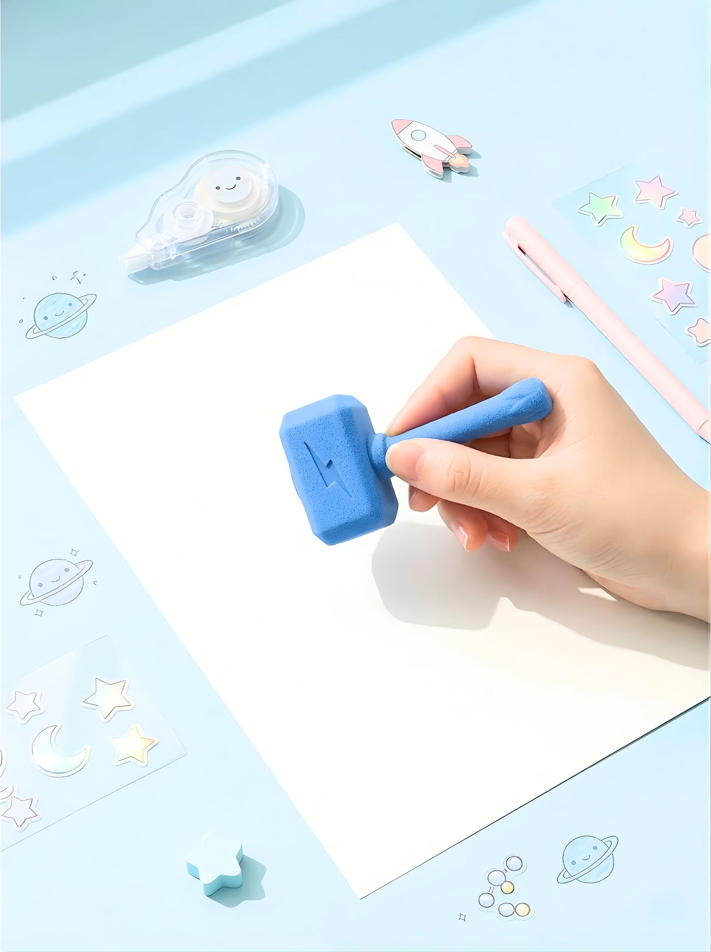 Hand holding a blue stamp over a piece of paper with decorative elements on a light blue background.