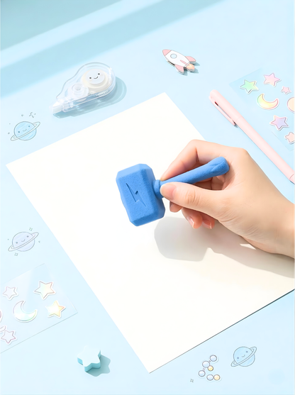 Hand holding a blue stamp over a piece of paper with decorative elements on a light blue background.