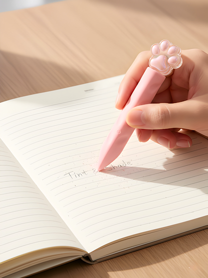 Hand holding a pink pen with a paw design, writing in an open notebook.
