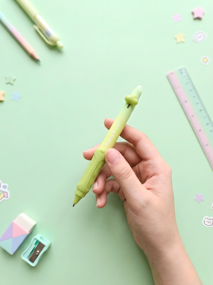 Hand holding a green mechanical pencil on a light green background with stationery items.