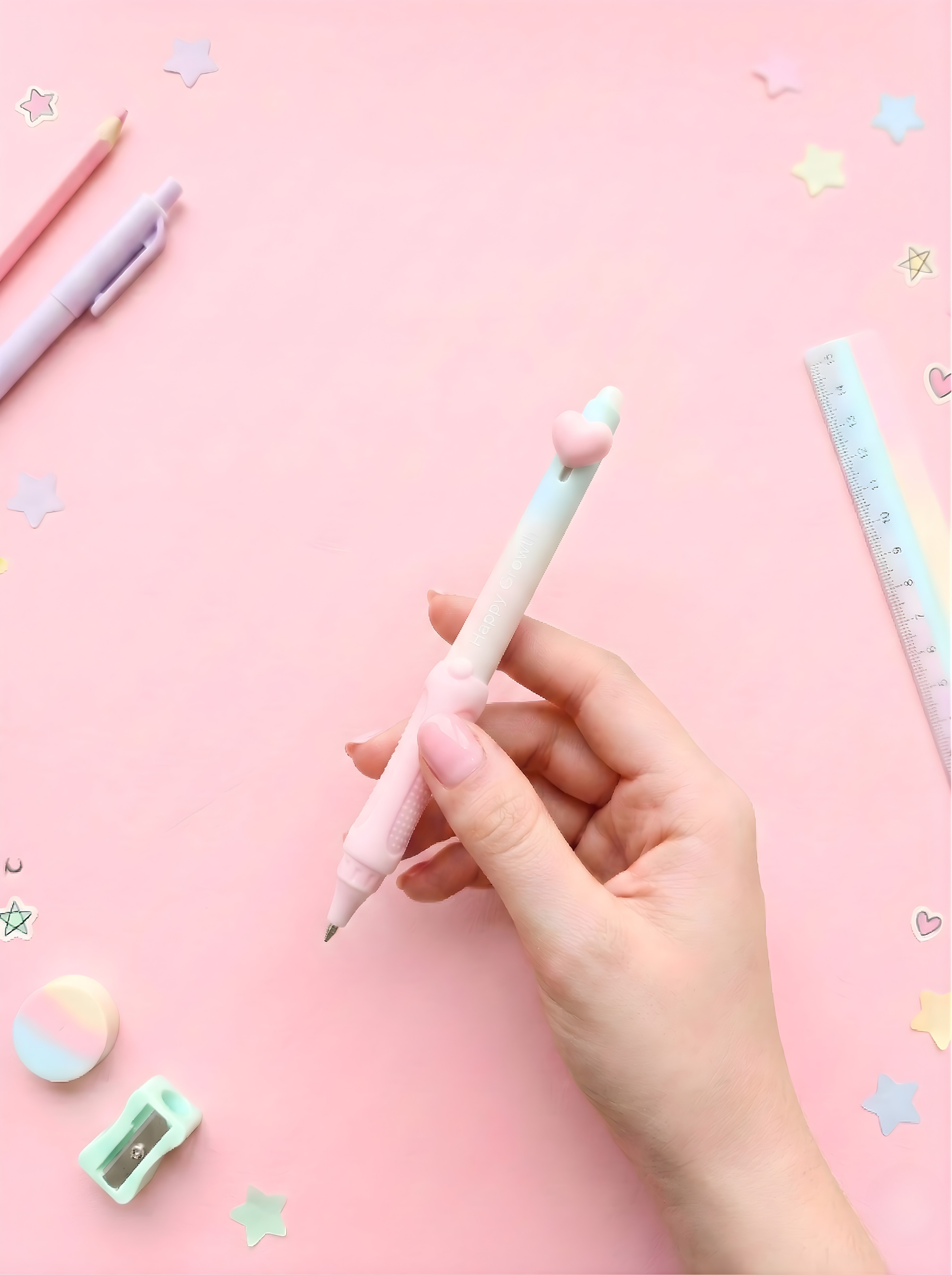Hand holding a light blue pen on a pink background with stationery items.