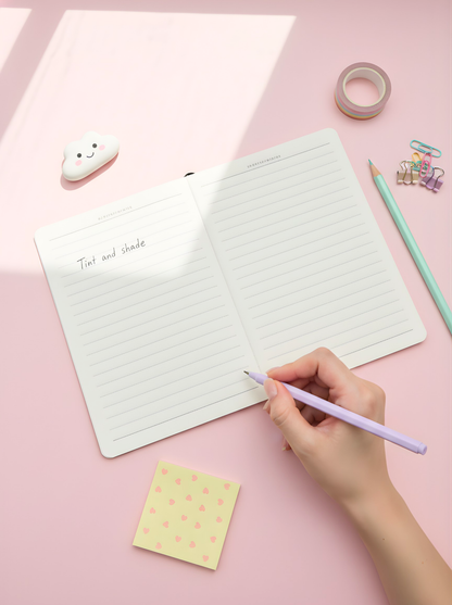 Hand writing in a notebook with stationery items on a pink background