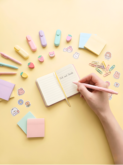Hand writing in a small notebook surrounded by stationery items on a yellow background