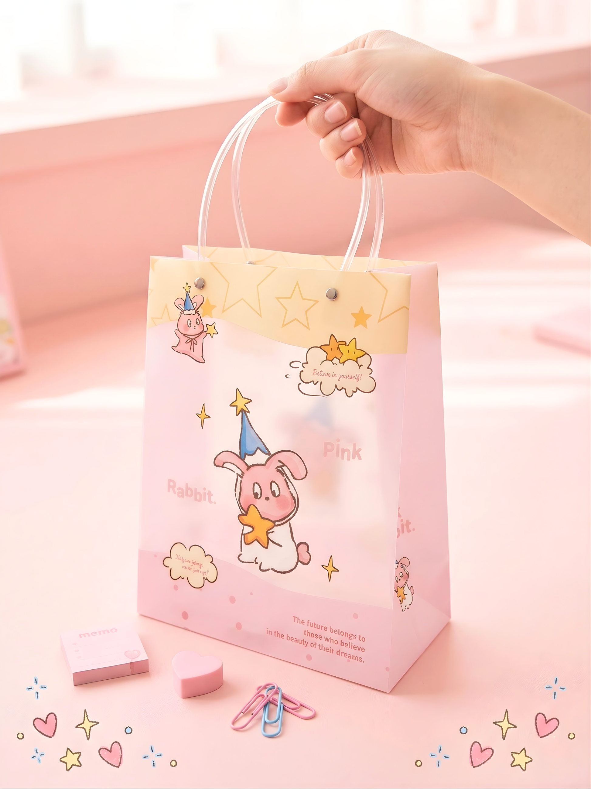 Pink gift bag with cartoon character and text, held by a hand on a light pink background.