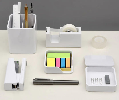 Collection of office supplies including a stapler, pen, tape dispenser, and sticky notes on a white surface.