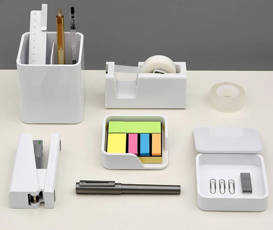 Collection of office supplies including a stapler, pen, tape dispenser, and sticky notes on a white surface.