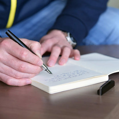 Person writing in a notebook with a pen on a wooden surface