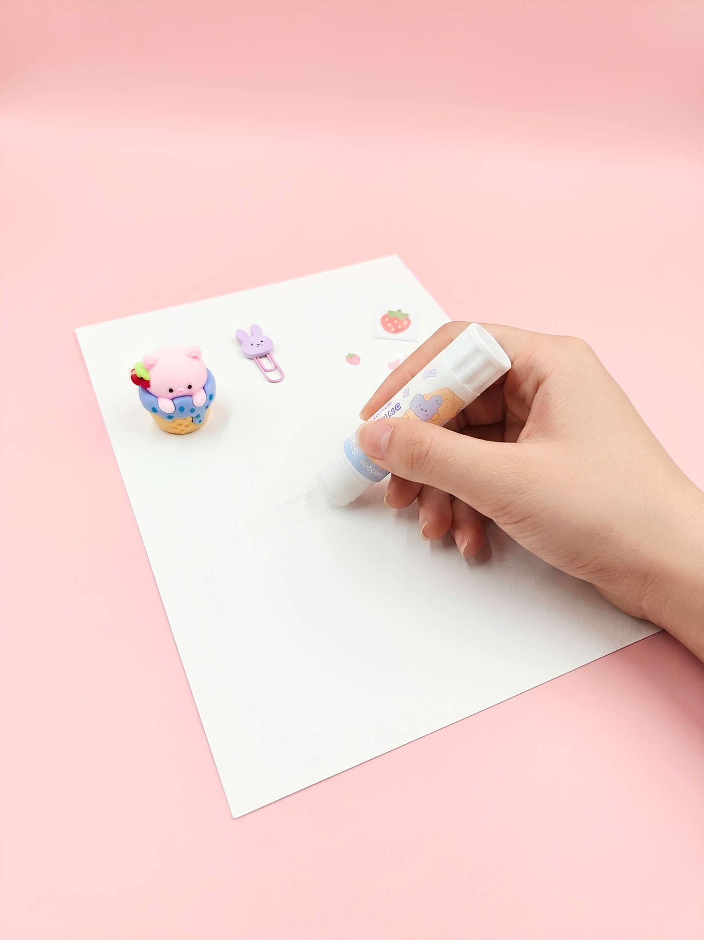 Hand using a small white eraser on a piece of paper with cartoon characters on a pink background